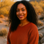 Smiling woman with voluminous natural curls wearing a burnt orange sweater, standing in a golden desert landscape during fall in Arizona